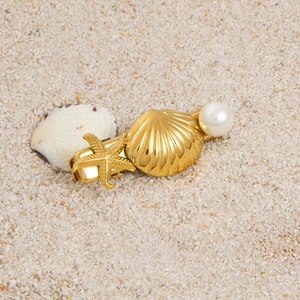 Detailed close-up of golden starfish and seashell hair clip with pearl on white sand