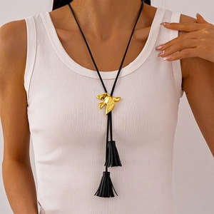 Close-up of golden bird slider and black leather fringe tassel on the long necklace
