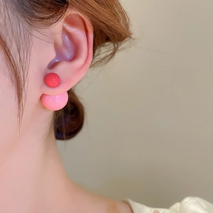 Close-up of dual-sided ball earrings featuring red and pink beads on a model