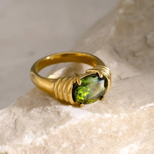 Detail of gold textured ring with a green oval gemstone on a natural stone base
