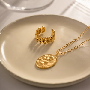 Close-up of golden olive leaf open ring and necklace set on a ceramic tray