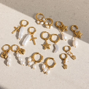 Golden hoop earrings set with baroque pearls, hearts, stars and cross charms on sand texture