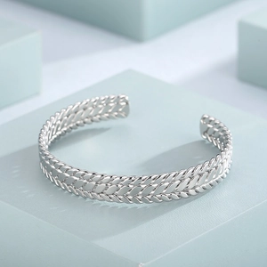 Macro detail of triple braided silver stainless steel open bangle on a geometric base