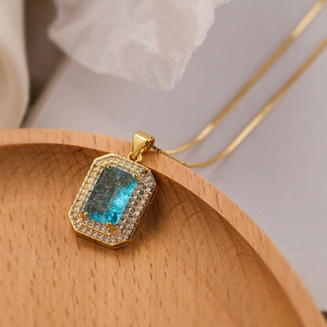 Close-up of 18K gold necklace with a rectangular blue gemstone pendant and zircon halo