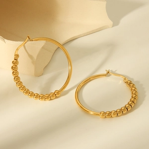 Macro detail of gold-plated ball bead hoop earrings on a minimalist stone surface