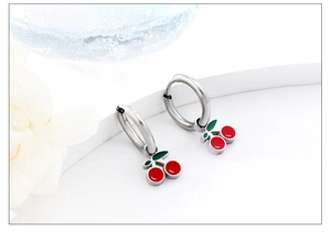 Detail of silver cherry earrings with red enamel charms on a minimalist white backdrop