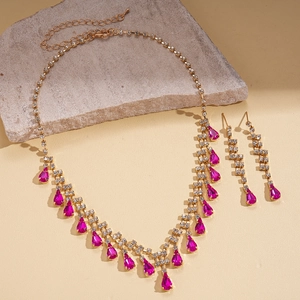 Elegant gold jewelry set with pink teardrop gems and tassels on stone background