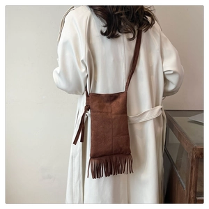 Detail of brown matte tote bag with tassels worn over a trench coat for casual look