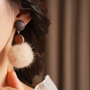 Detail of round wood and beige pompom earring showing plush texture and gold metal accents