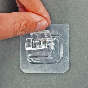 Self-adhesive transparent curtain rod holder hook being installed on a grey textured wall