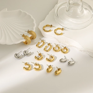 Detailed close-up of 18K gold and silver geometric hoop earrings on a shell tray