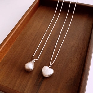 Détail de colliers cœur et goutte en argent brossé mat posés sur un plateau en bois