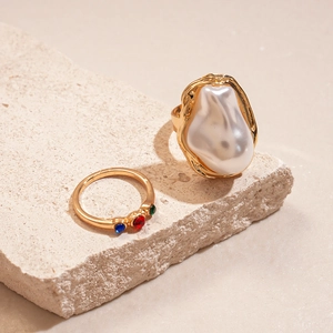 Detail of gold rings with baroque pearl and colorful gemstones on stone background