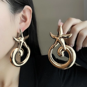 Detail of oversized gold earrings featuring a starfish design and large spiral hoop