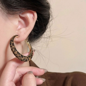 Macro view of wide leopard print hoop earring with golden metal trim on model