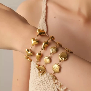 Detail showing layered gold bracelets with heart and shell charms on model's wrist
