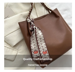 Close-up of brown leather tote bag with woven handles and printed silk scarf detail