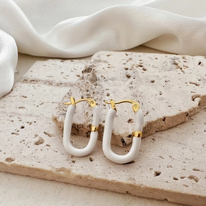 Detailed macro of gold and white U-shaped enamel hoop earrings on stone background