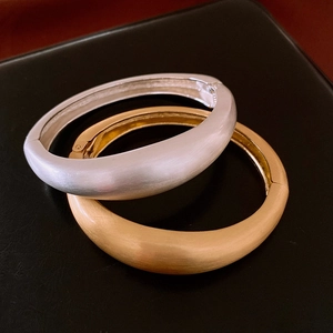 Détail de bracelets ouverts en métal brossé mat, or et argent, avec mécanisme de charnière