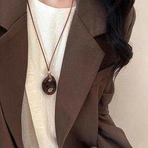 Macro view of brown resin oval pendant with hollow details on a minimalist wax cord