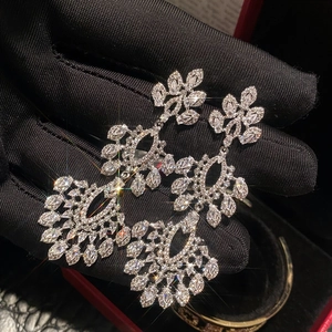 Détail de boucles d'oreilles à pompons en zircon brillant tenues par un gant noir