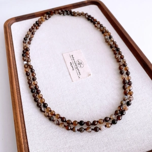 Detailed close-up of dark agate beaded necklace with faceted round stones on wood tray