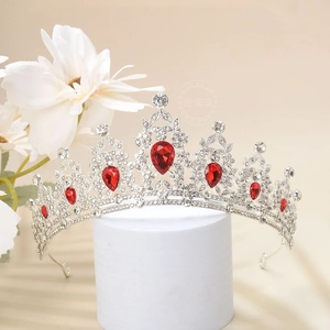 Detailed view of silver luxury crown with red teardrop rhinestones on white pedestal
