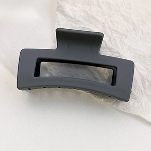 Detail of matte black rectangular hollow hair claw clip on white textured background