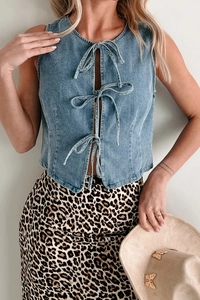 Detail of light blue denim vest showing front lace-up ribbon bows and trendy texture
