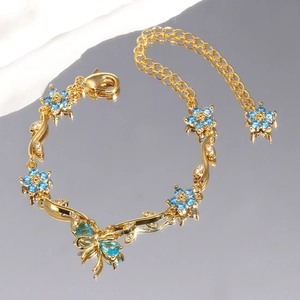 Makroaufnahme von goldenem Rebenarmband mit blauen Zirkonia-Blumen und Schmetterling