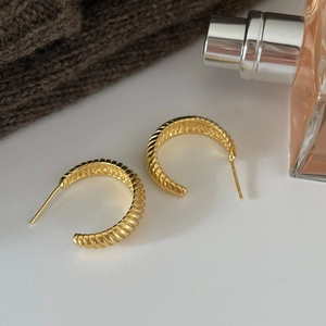 Macro detail of gold-plated C-shape hoop earrings with S925 hallmark and twisted texture