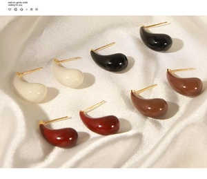Detail shot of teardrop enamel earrings in cream, black, mocha, and red on white silk