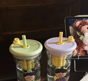 Detail of cartoon glass tumblers with tea infuser, colorful silicone lids and straws