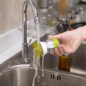 Kitchen dish soap dispensing brush with green handle and clear reservoir in water
