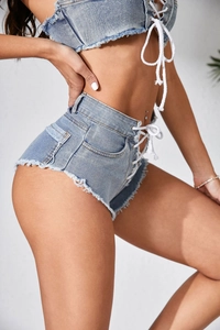 Dettaglio degli shorts in denim azzurro a vita alta con lacci laterali e bordi sfrangiati