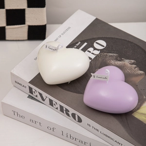Romantic heart-shaped scented candles in cream and purple colors on decorative books