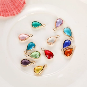 Set of twelve multi-color birthstone pendants in gold teardrop frames on a white ceramic plate