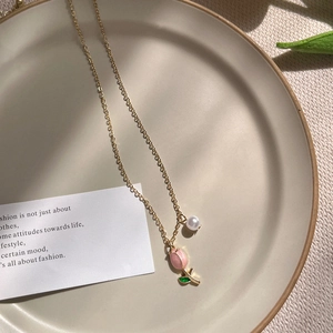 Elegant gold necklace featuring pink tulip pendant and white pearl on ceramic tray