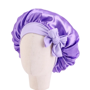 Dettaglio di una cuffia da notte in raso viola per neonati con fiocco decorativo su modella