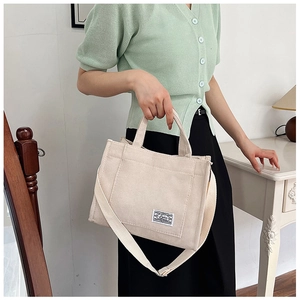 Detail of beige corduroy tote bag showing woven texture, strap, and designer label tag