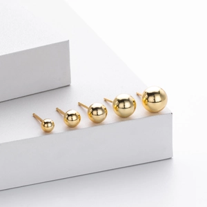 Detailed view of polished golden ball stud earrings in five sizes on white display stand