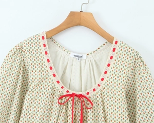 Detail van de vierkante halslijn met rode strik op een beige bloemenjurk