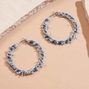 Close-up of geometric hoop earrings wrapped in blue and white frayed denim fabric