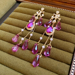 Detail of drop tassel earrings with purple crystals and pearls on green velvet