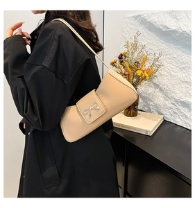 Fashionable beige underarm bag with a golden bow detail worn with a black coat