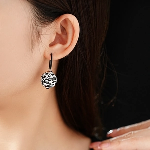 Detail of leopard print sphere earring on black hoop worn by a model in close-up shot