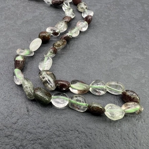 Macro shot of irregular green phantom quartz beads on a textured grey stone background