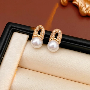 Gros plan sur des boucles d'oreilles en U dorées avec zircons et perles blanches