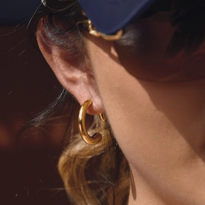 Gros plan de boucles d'oreilles créoles C épaisses en acier doré 18K sur l'oreille