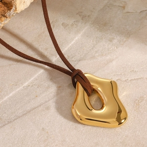 Macro detail of a golden irregular liquid pendant on suede cord over marble surface